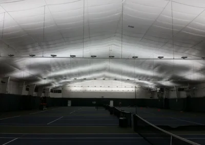 Indoor tennis courts with overhead lighting in an enclosed, air-supported structure.