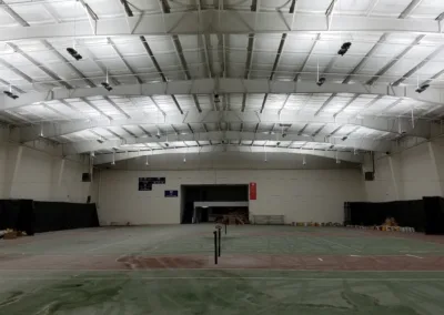 An empty indoor sports court with materials stacked at one end under bright artificial lighting.