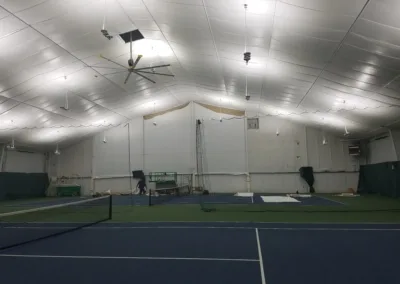 Indoor tennis court facility with artificial lighting and a person in the distance.