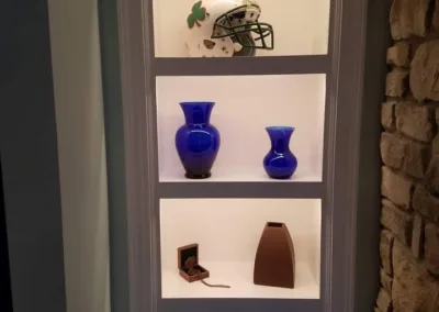 A three-shelf display featuring a helmet on the top shelf, two blue vases on the middle shelf, and a clock and an iron-shaped object on the bottom shelf.