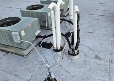 Image of a rooftop with two HVAC units and multiple PVC pipes connected to them, surrounded by a white, sealed roofing material.